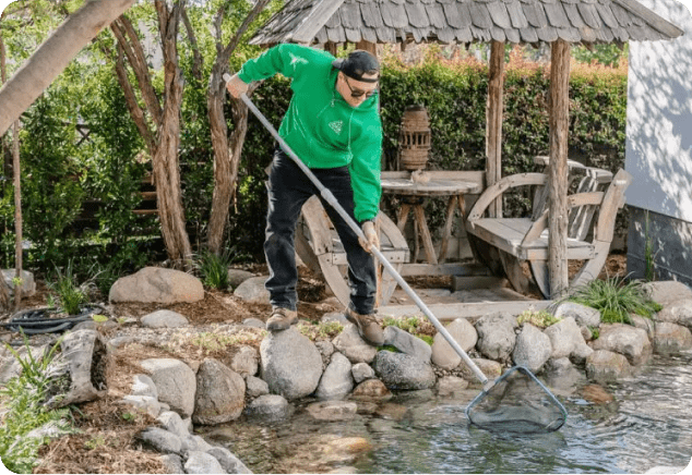 A man wearing a green hoodie cleaning a pond